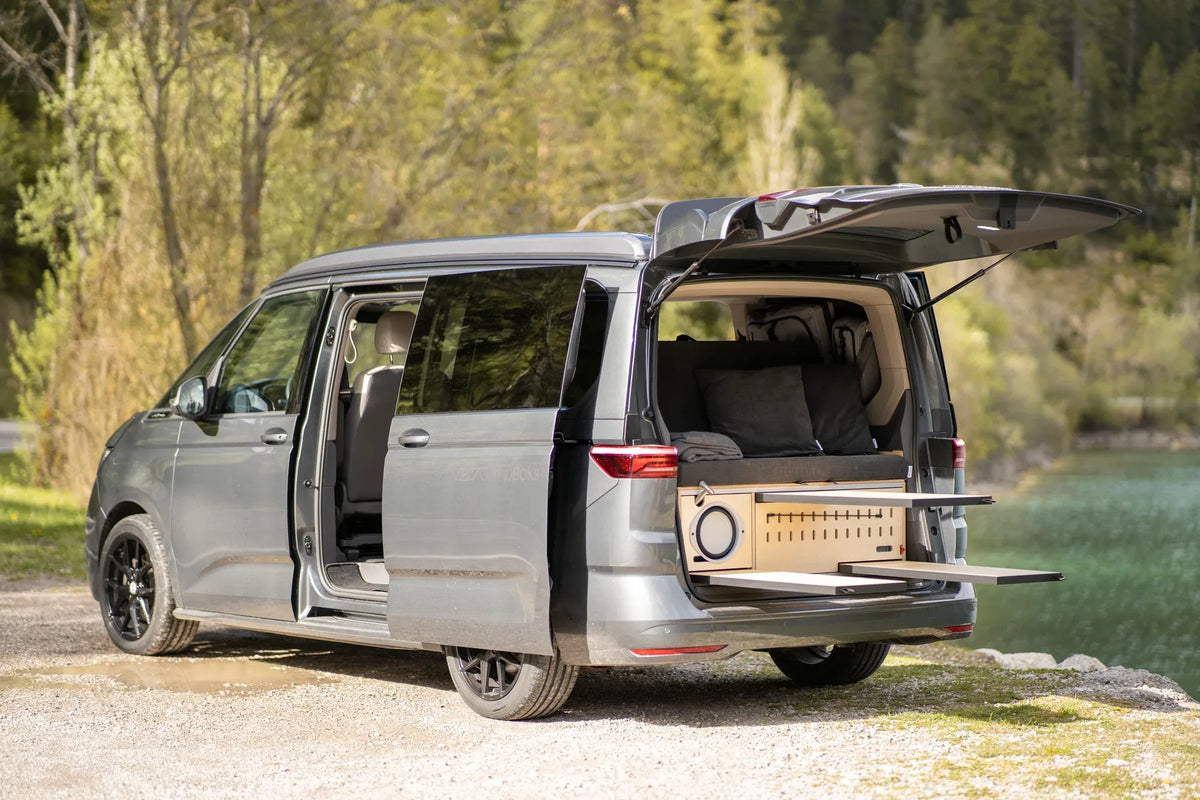 Grauer Campervan mit CampBoks, geöffneter Schiebetür und offener Heckklappe am See.